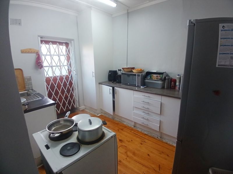 A functional kitchen featuring white cabinetry, laminate countertops, a stainless steel sink, and timber flooring, with direct access to an exterior security door.