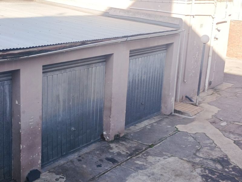 An elevated view of a multi-bay garage structure featuring metal doors and a corrugated roof, showing signs of significant exterior wear and weathering.