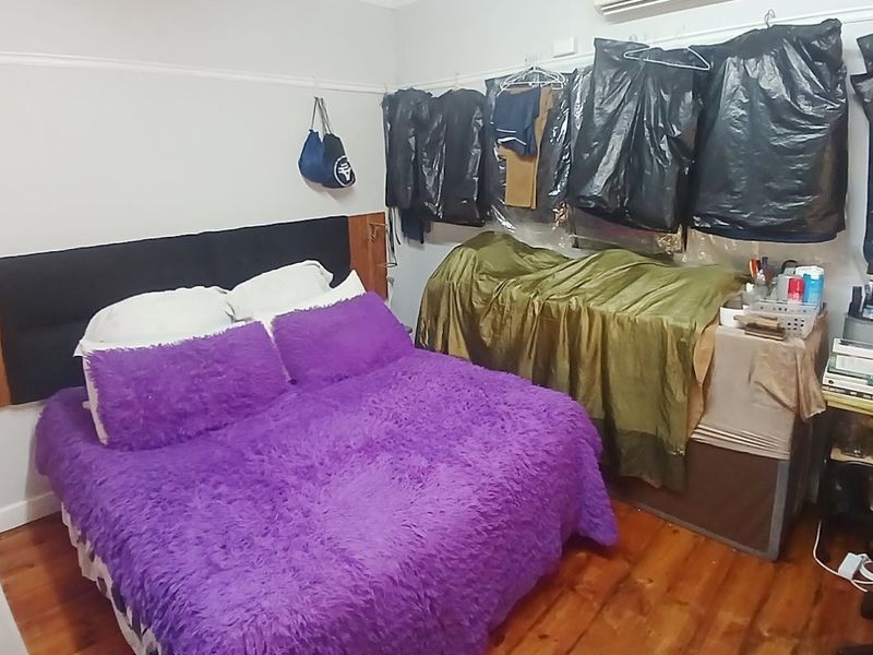 A bedroom featuring timber flooring, a picture rail, and a wall-mounted air conditioning unit.