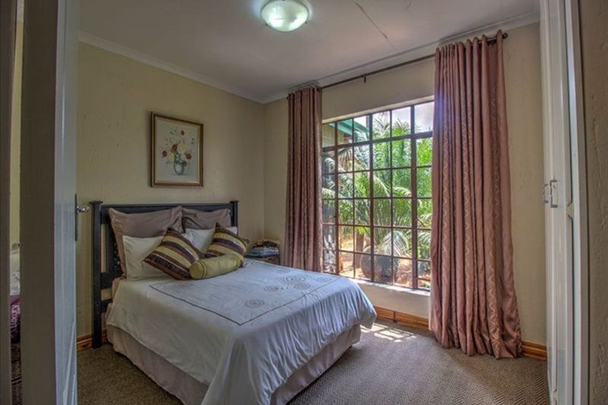 A cozy bedroom featuring built-in cupboards, a large window with garden views, and neutral carpeting.