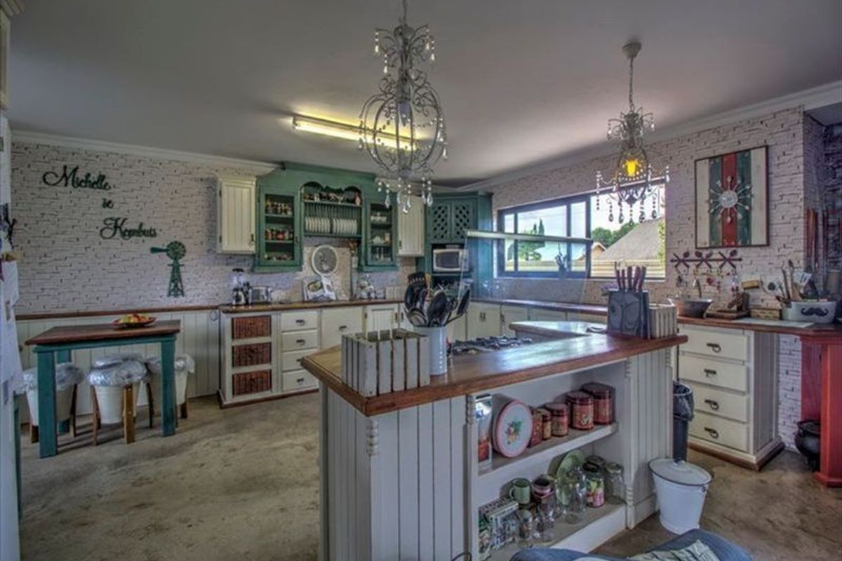 A rustic-style kitchen featuring built-in cabinetry, a central island with a wooden countertop, and decorative chandeliers, set against a textured brick-style wall.