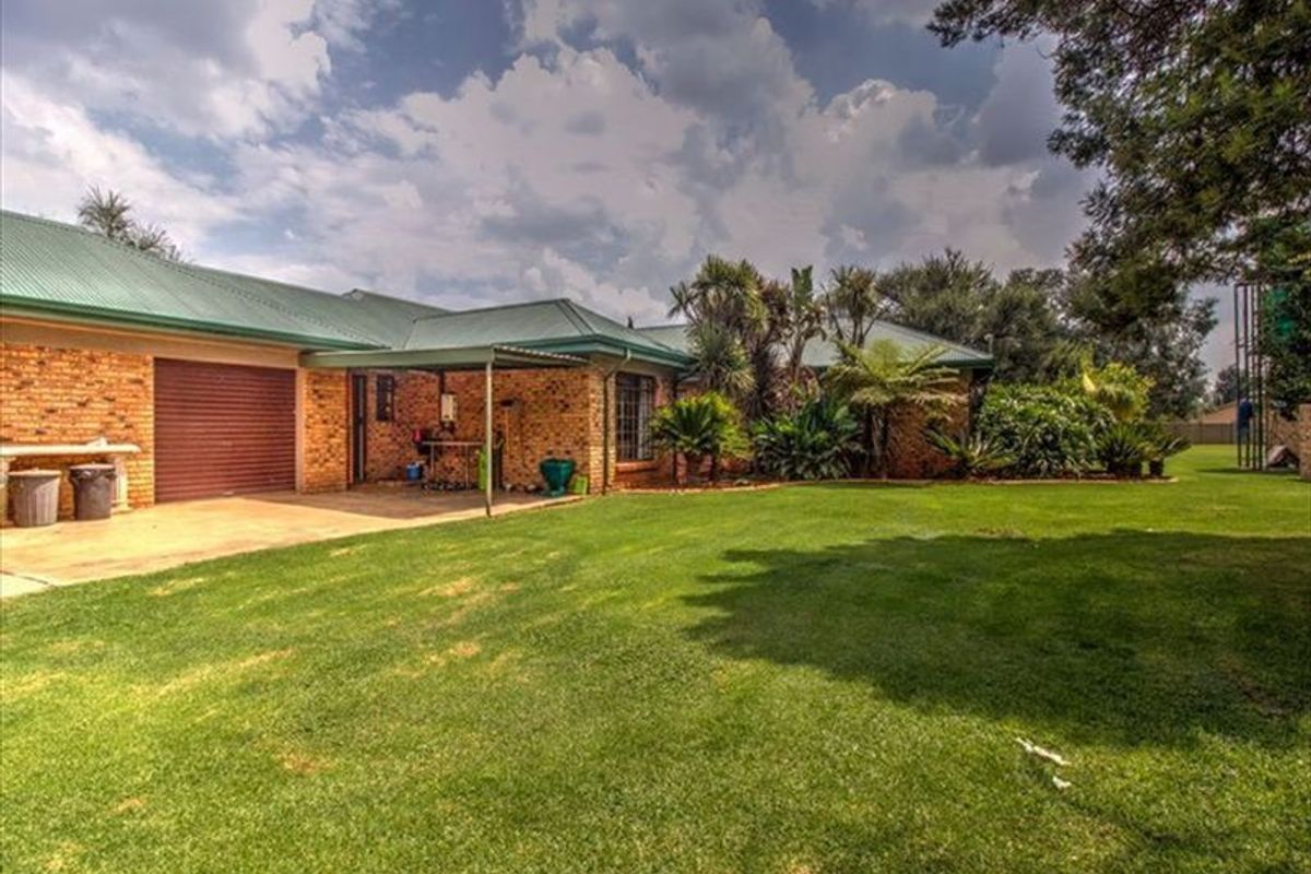 A view of the rear exterior of the property featuring a brick facade, metal roofing, a covered patio area, and a well-maintained lawn.