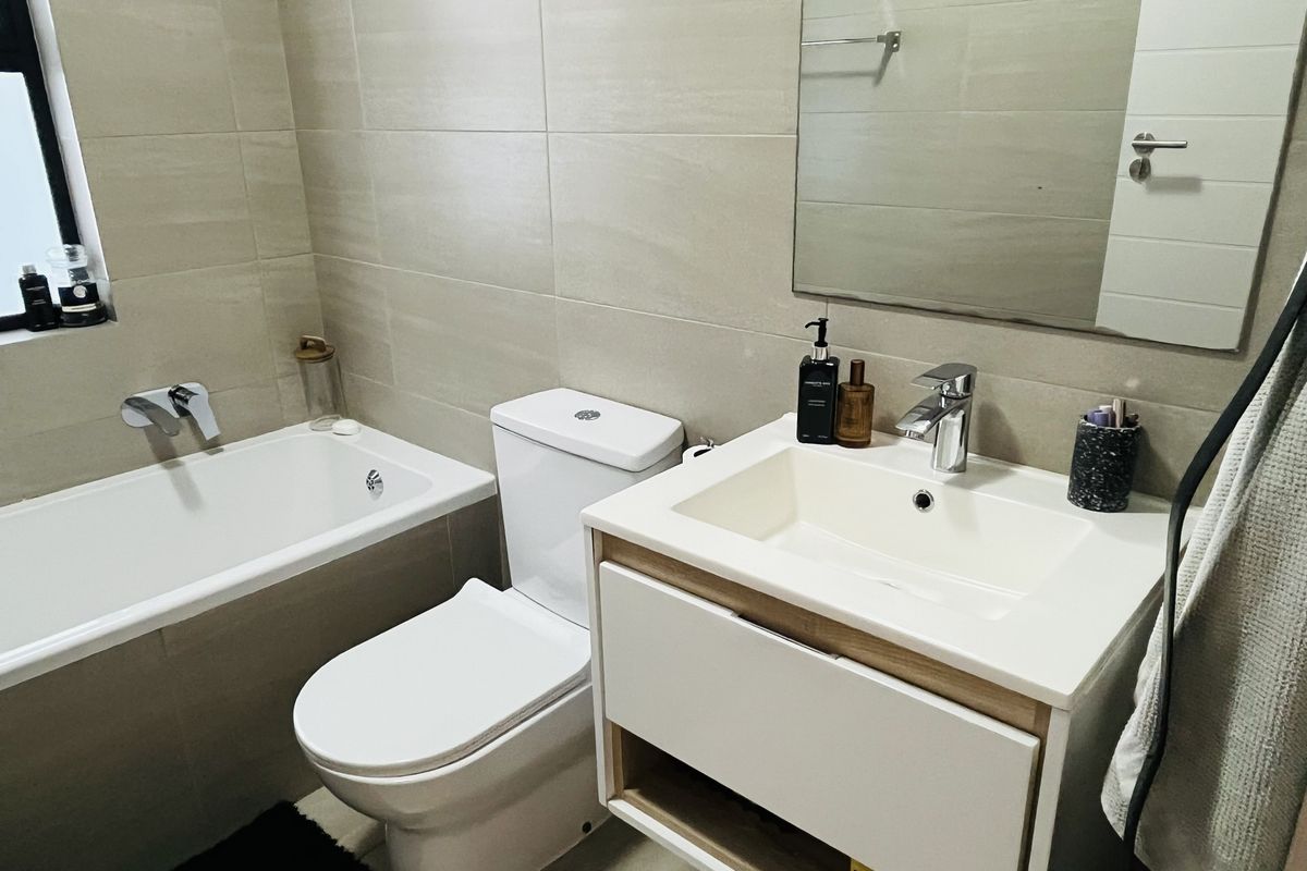 A modern bathroom featuring a built-in bathtub, a sleek vanity with an integrated basin, and neutral wall tiling.