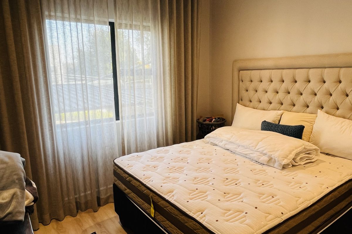A well-maintained bedroom featuring light laminate flooring, neutral walls, and a large tufted headboard, complemented by floor-to-ceiling curtains.