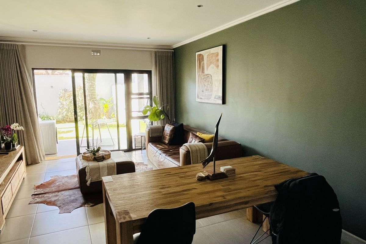 A well-lit living area featuring large sliding glass doors that open to an outdoor space, complemented by neutral tiled flooring and a feature wall.