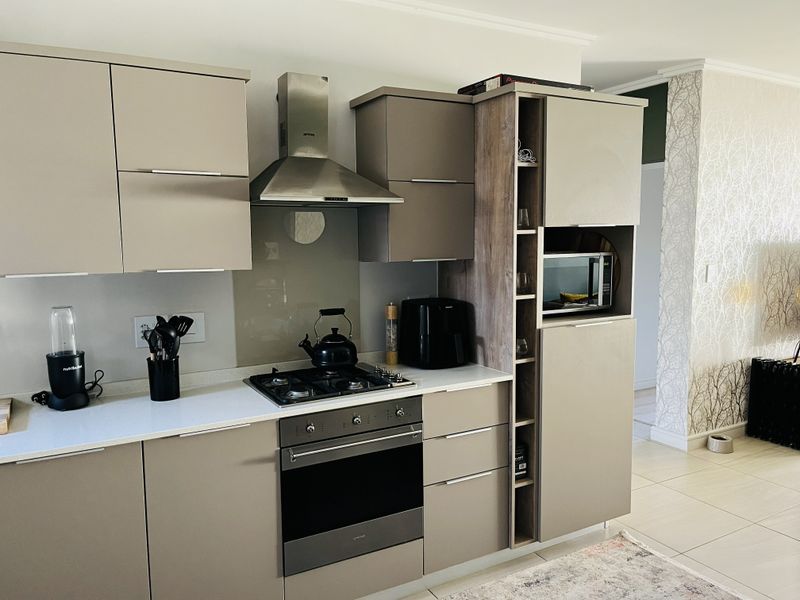 Modern kitchen featuring sleek taupe cabinetry, stone countertops, a gas hob, extractor fan, and integrated oven with built-in microwave.
