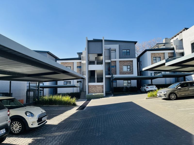 Exterior view of a modern apartment complex featuring paved parking areas, covered carports, and contemporary building facade with stone accents.