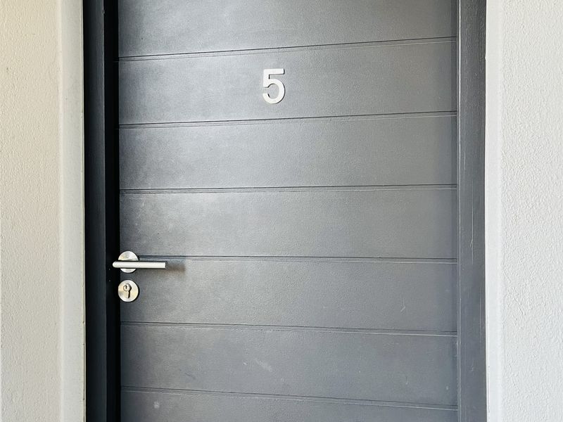 A clean, modern apartment entrance door finished in dark grey with horizontal panel detailing and a brushed metal handle.