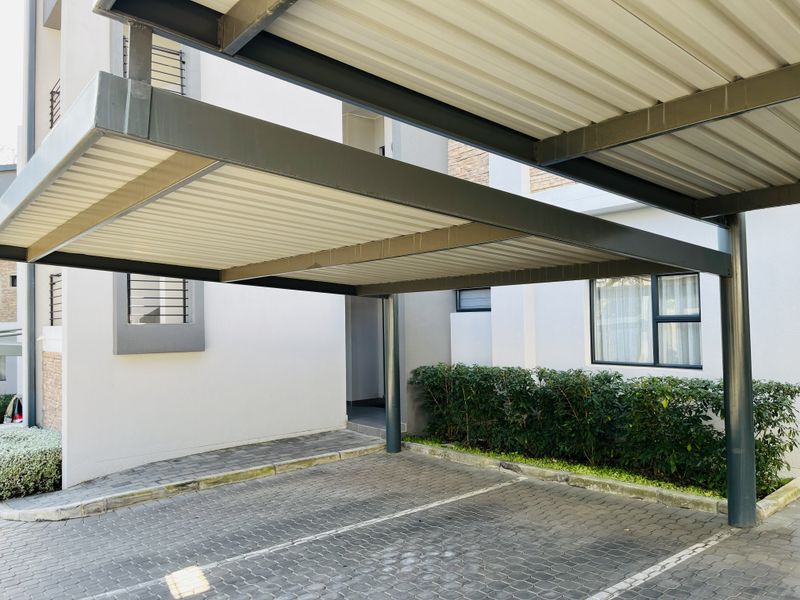 A well-maintained covered carport area with paved driveway and modern steel structure, providing dedicated parking space for the apartment.