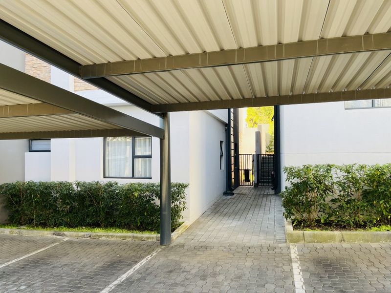 A well-maintained covered carport area with paved driveway and a secure pedestrian walkway leading to the apartment entrance.