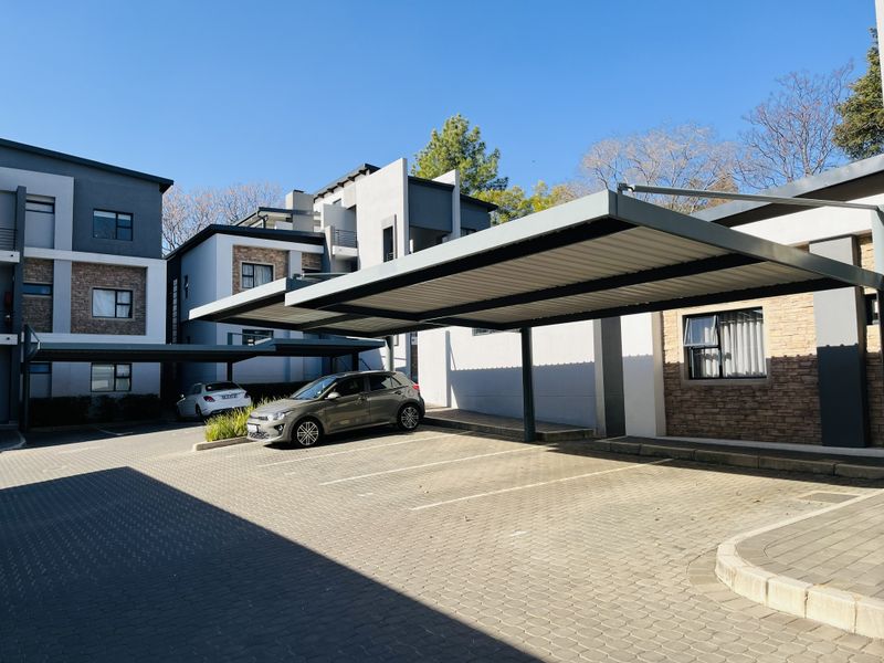 Exterior view of the apartment complex featuring covered parking bays, paved driveway, and modern building facade with stone cladding accents.