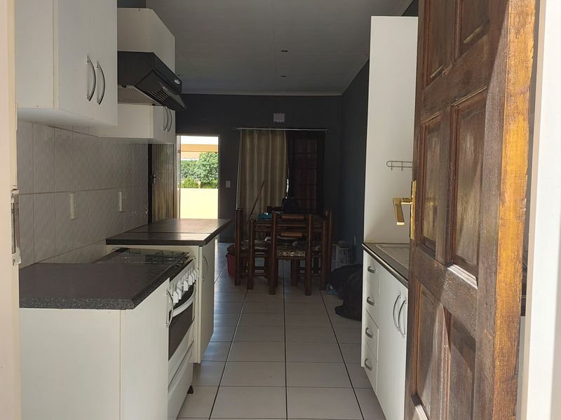 Open-plan kitchen and dining area featuring tiled flooring, built-in cabinetry, and a gas stove, leading towards an outdoor space.