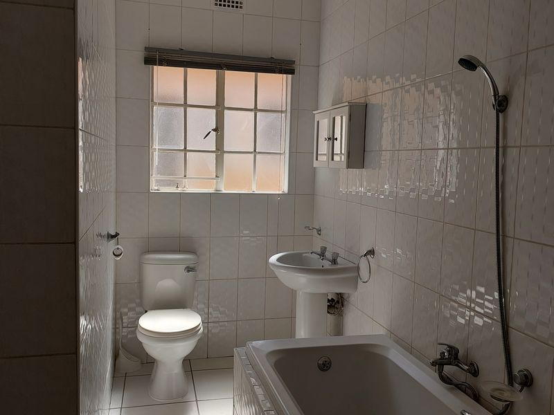 A functional bathroom featuring a pedestal basin, toilet, and bathtub with a handheld shower attachment, finished with white wall and floor tiles.