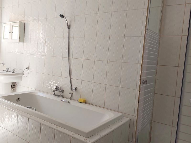 A functional bathroom featuring a built-in bathtub, separate shower enclosure, and pedestal basin with classic white wall tiling.