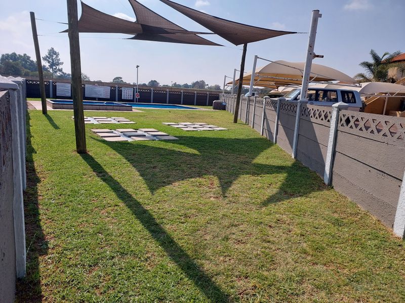 Communal outdoor pool area featuring a swimming pool, shade sails for sun protection, and a secure precast concrete boundary wall.