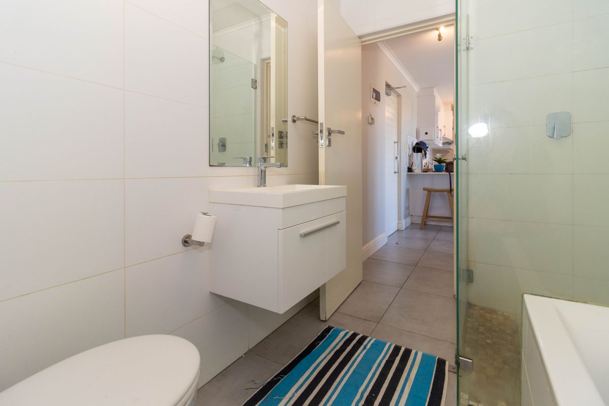A functional bathroom featuring a wall-mounted vanity, basin, toilet, and a glass-enclosed shower with neutral wall and floor tiling.