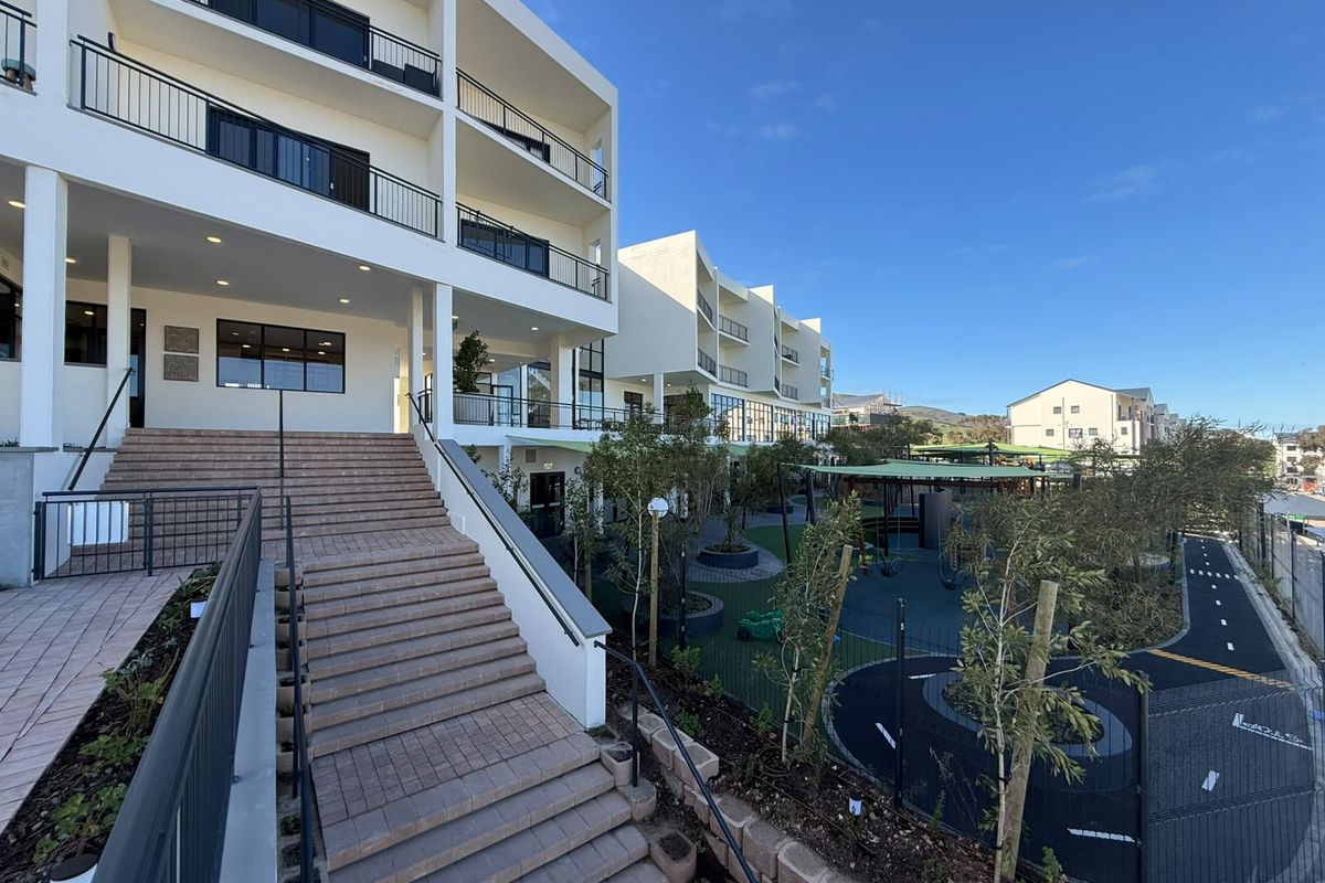 Exterior view of a modern apartment complex featuring a central staircase, multi-level balconies, and landscaped communal outdoor areas.