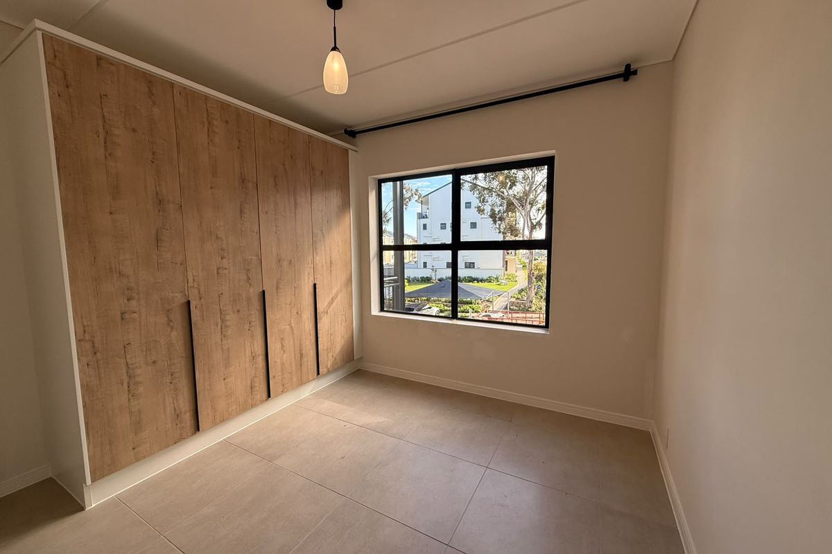 A bright, modern bedroom featuring large-format floor tiles, a spacious built-in wardrobe with wood-grain finish, and a black-framed window.