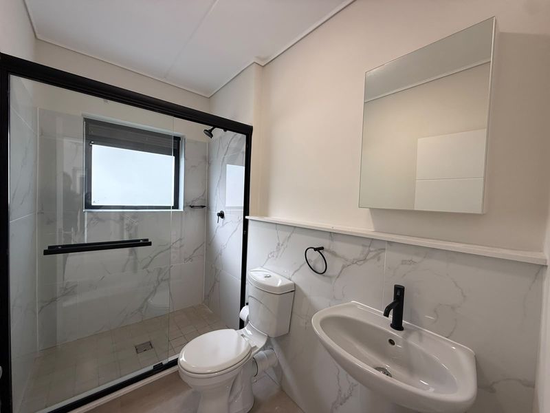 Modern bathroom featuring a walk-in shower with black-framed glass, marble-look wall tiles, a pedestal basin with black fixtures, and a wall-mounted mirror.