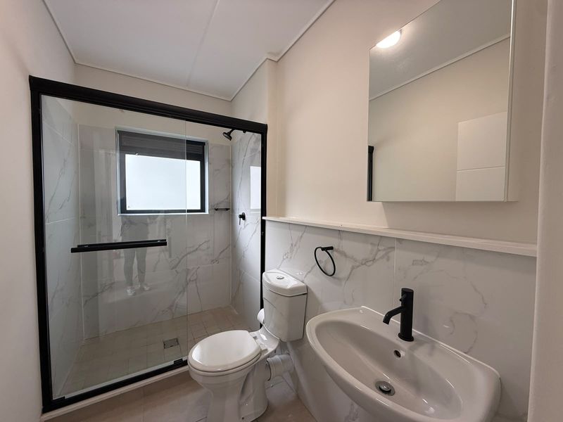 Modern bathroom featuring a walk-in shower with black frame, marble-look wall tiles, pedestal basin with black tapware, and a wall-mounted mirror.