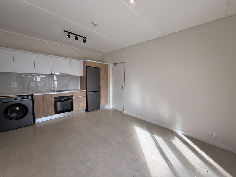 Modern open-plan kitchen featuring sleek wood-tone and white cabinetry, integrated appliances, stone-look backsplash, and neutral tiled flooring in a bright, contemporary apartment space.