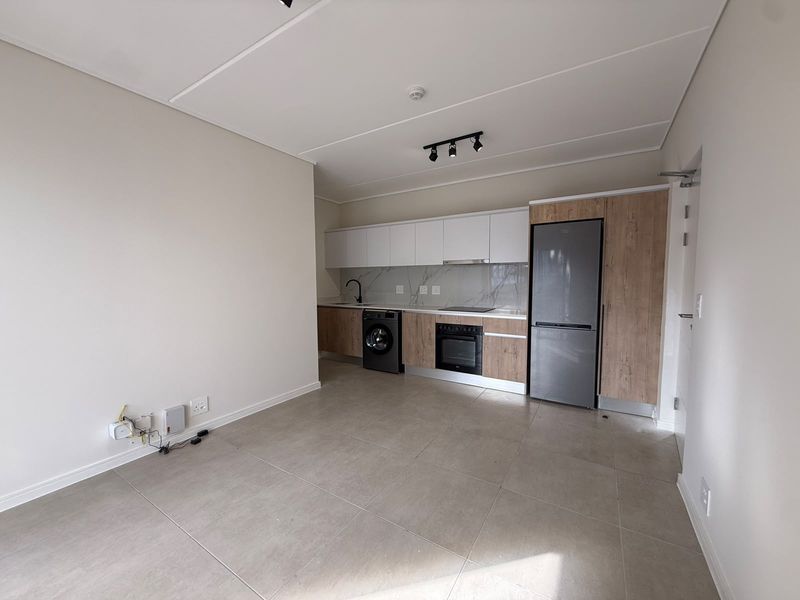 Modern open-plan kitchen featuring sleek two-tone cabinetry, integrated appliances, stone-look backsplash, and neutral tiled flooring in a bright, contemporary apartment setting.