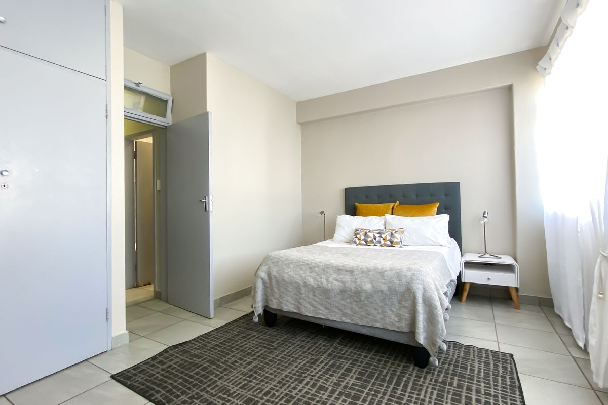 A well-lit bedroom featuring neutral walls, tiled flooring, and built-in cupboards, offering a clean and functional living space.
