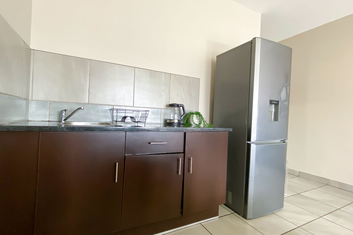 A compact kitchen area featuring dark brown cabinetry, a stainless steel sink, tiled splashback, and neutral floor tiles.