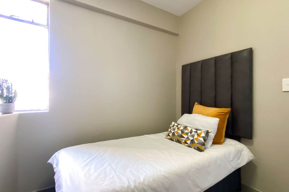 A compact bedroom featuring a neutral color palette and a tall, dark upholstered headboard.