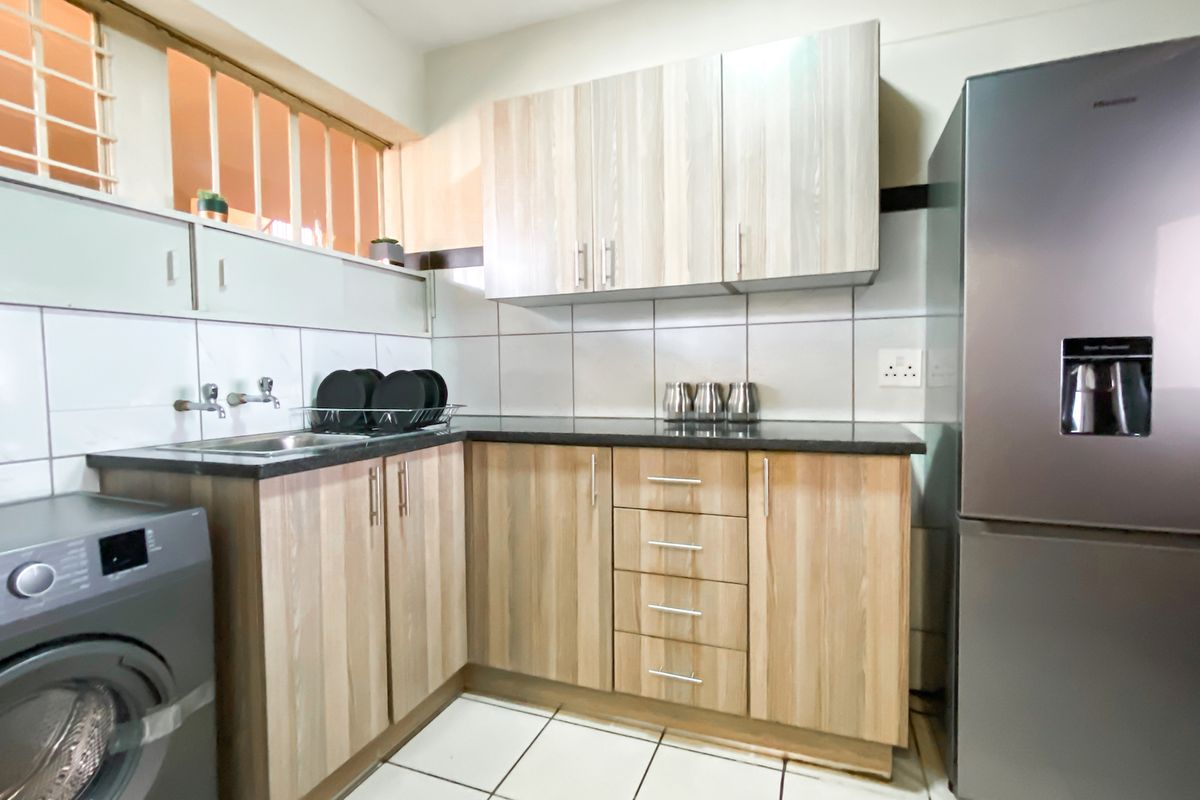 A functional kitchen featuring light wood-grain laminate cabinetry, granite countertops, a stainless steel sink, and clean tiled finishes.