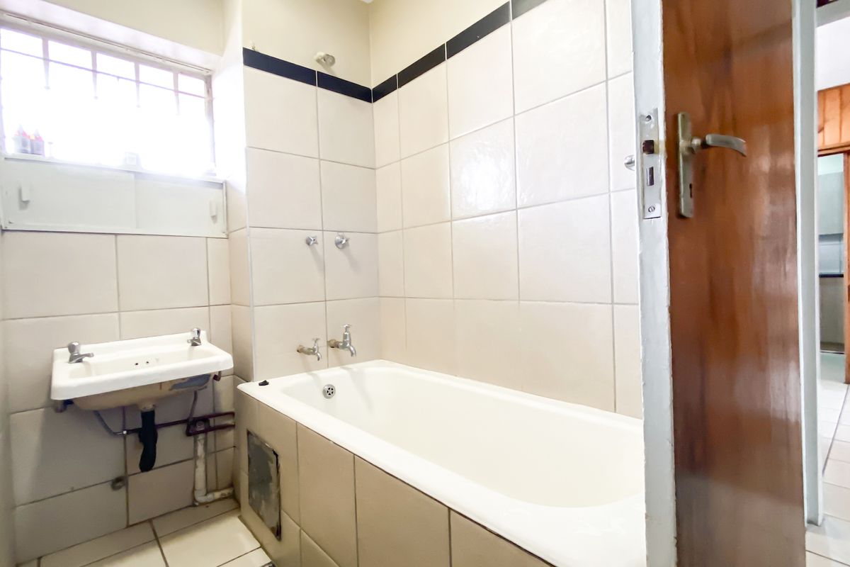 A dated bathroom featuring a built-in bathtub, wall-mounted basin, and neutral ceramic tiling, requiring cosmetic updates to modernize the space.