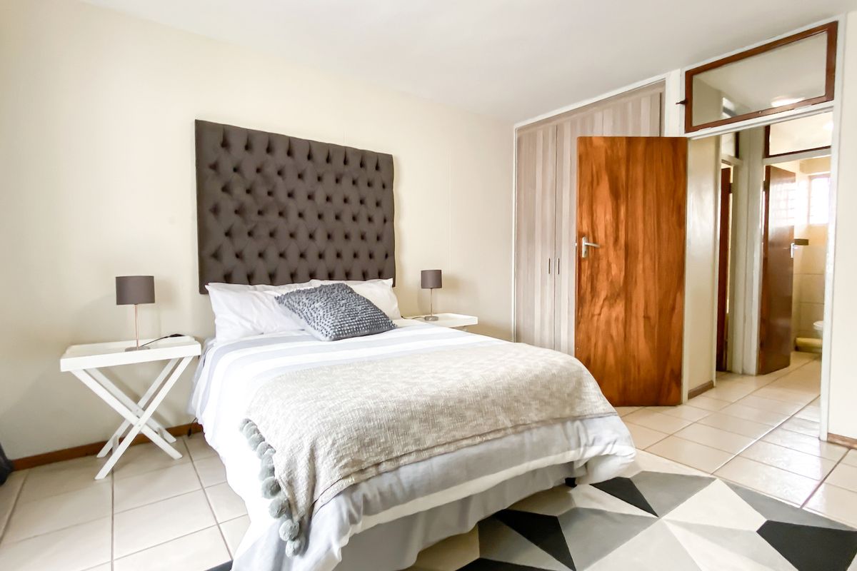 A well-lit bedroom featuring tiled flooring, built-in cupboards, and a wooden door leading to an adjacent space.