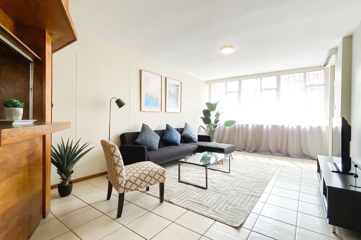 A bright living room featuring tiled flooring, a large window allowing natural light, and a built-in wooden bar counter.