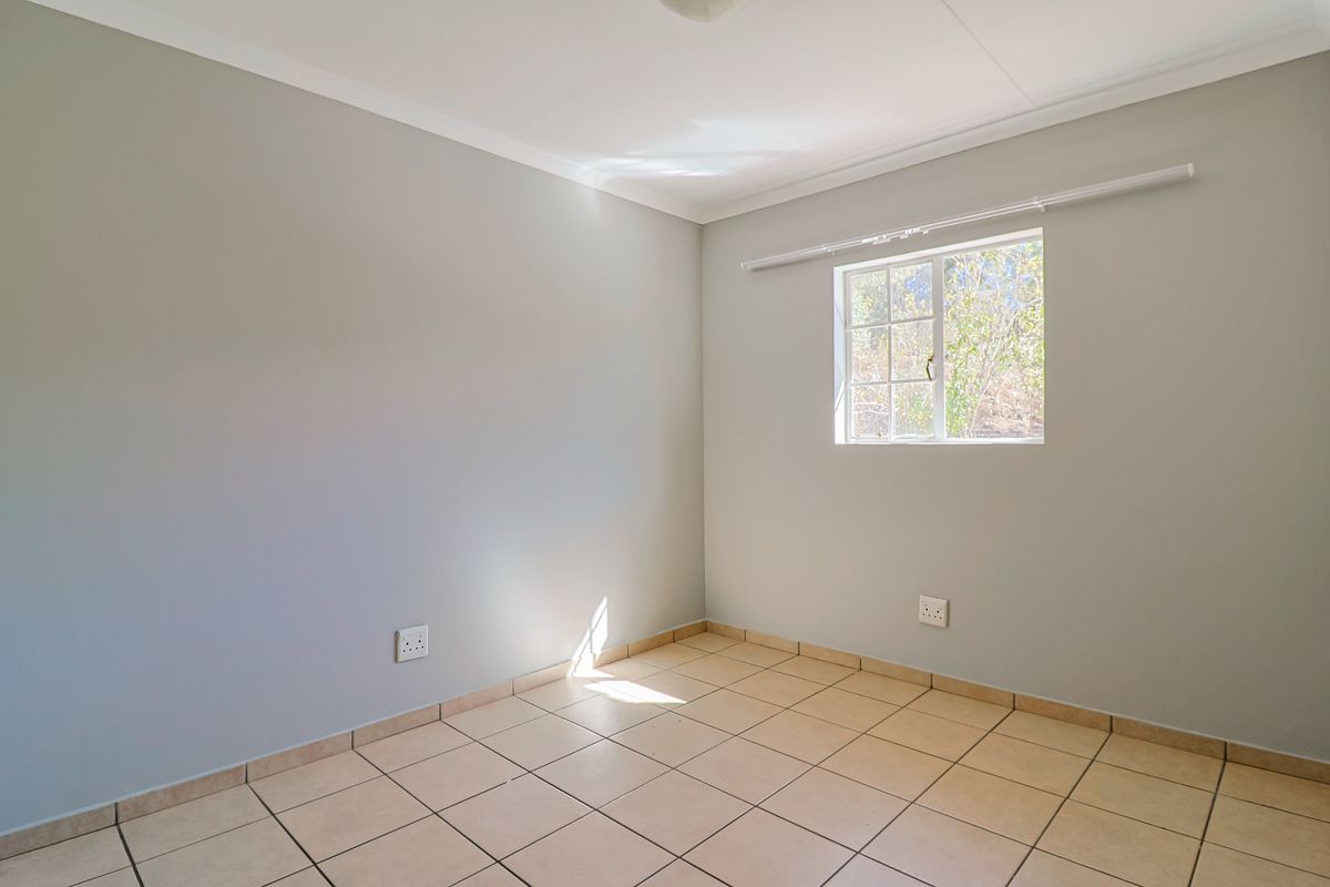 A clean, empty bedroom featuring neutral wall paint, tiled flooring, and a window providing natural light.