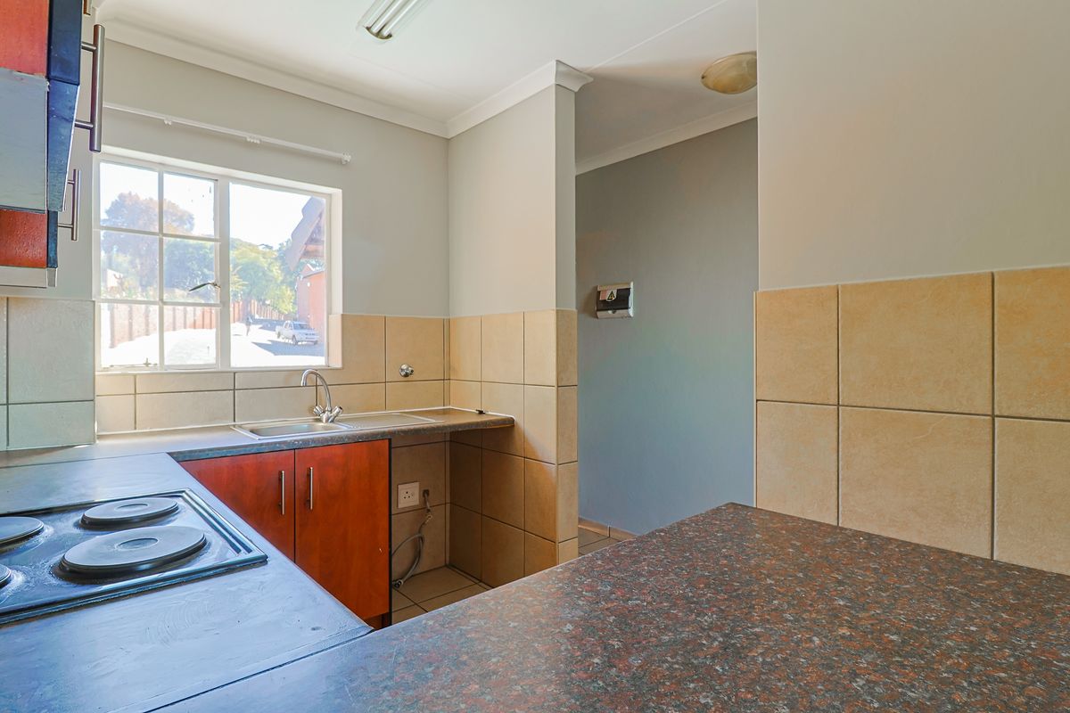 A functional kitchen featuring built-in cabinetry, laminate countertops, a stainless steel sink, and an integrated electric hob with tiled backsplash.
