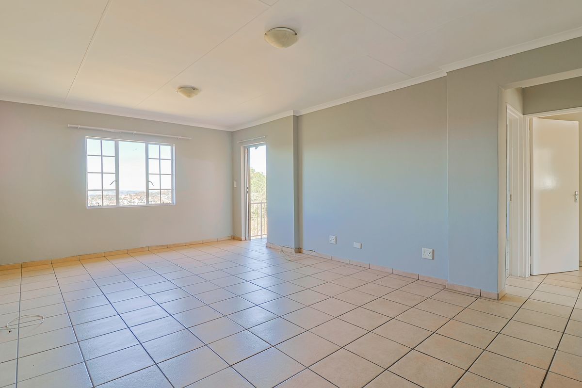 A spacious, empty living area featuring neutral tiled flooring, ample natural light from grid pane windows, and direct access to a balcony.