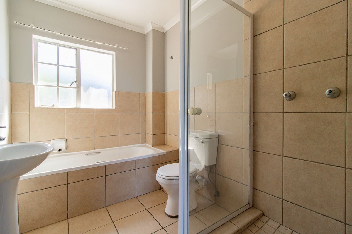 A functional bathroom featuring a pedestal basin, built-in bathtub, and a separate shower enclosure with tiled finishes throughout.