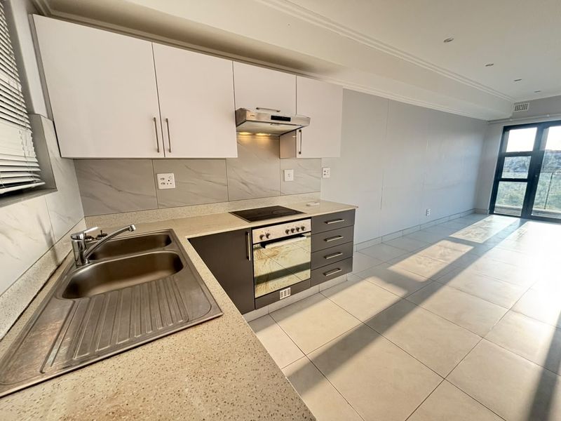 Modern open-plan kitchen featuring sleek cabinetry, stone countertops, integrated appliances, and tiled flooring, flowing into a bright living area with balcony access.