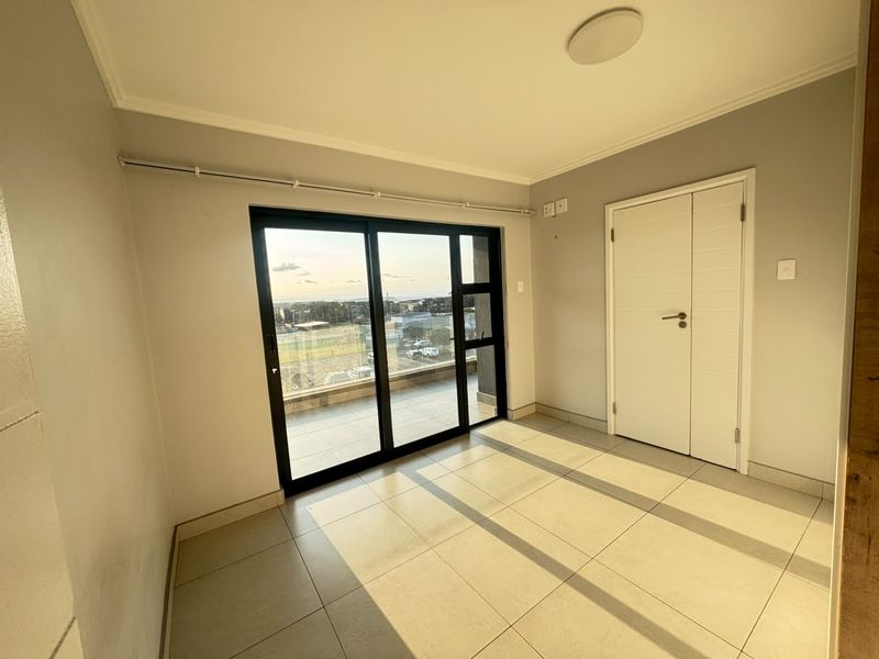A bright, empty bedroom featuring tiled flooring, a built-in cupboard, and a large sliding glass door providing access to a balcony.
