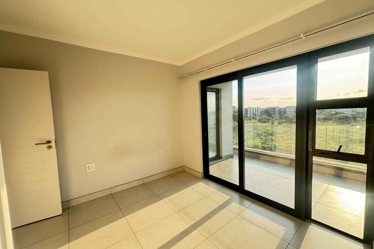 A bright, empty bedroom featuring large sliding glass doors that open onto a private balcony, offering natural light and tiled flooring throughout.