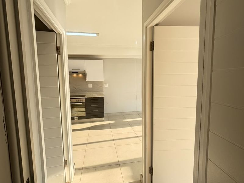 A view from the hallway looking into an open-plan kitchen area featuring modern cabinetry, built-in appliances, and neutral tiled flooring throughout.