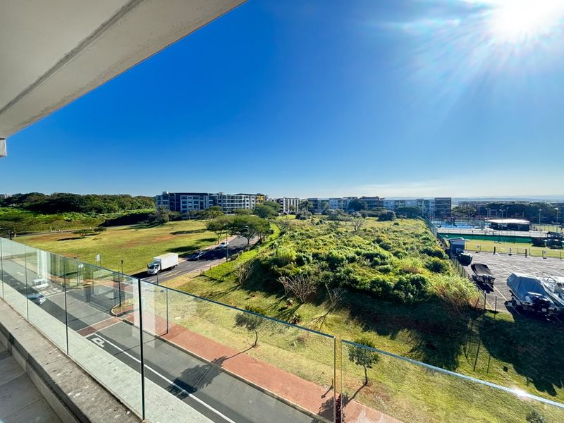 A spacious balcony featuring a modern glass balustrade, offering expansive elevated views over the surrounding estate and landscape.