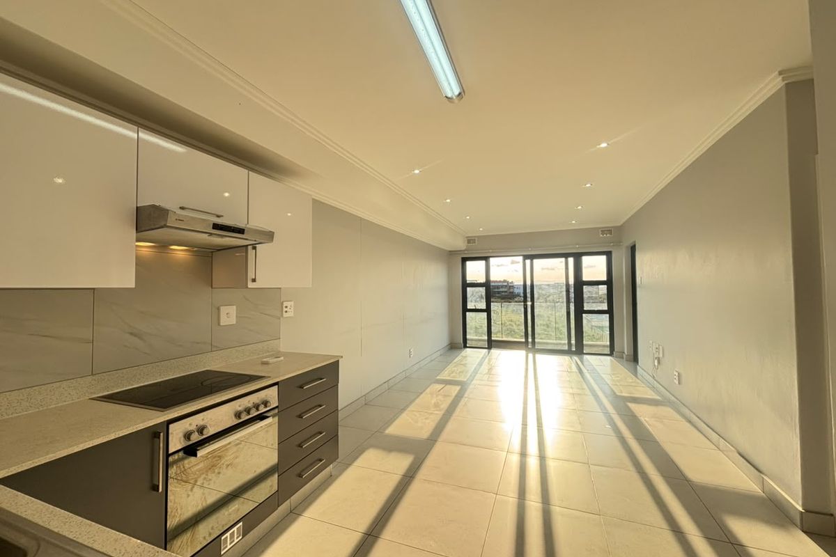 Modern open-plan kitchen and living area featuring sleek cabinetry, integrated appliances, tiled flooring, and large sliding doors leading to an outdoor space.