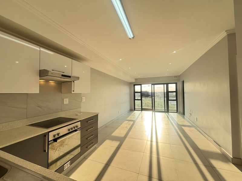 Modern open-plan kitchen and living area featuring sleek cabinetry, integrated appliances, tiled flooring, and large sliding doors leading to an outdoor space.