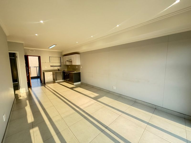 An open-plan living and kitchen area featuring tiled flooring, recessed lighting, and a compact built-in kitchen with integrated appliances.