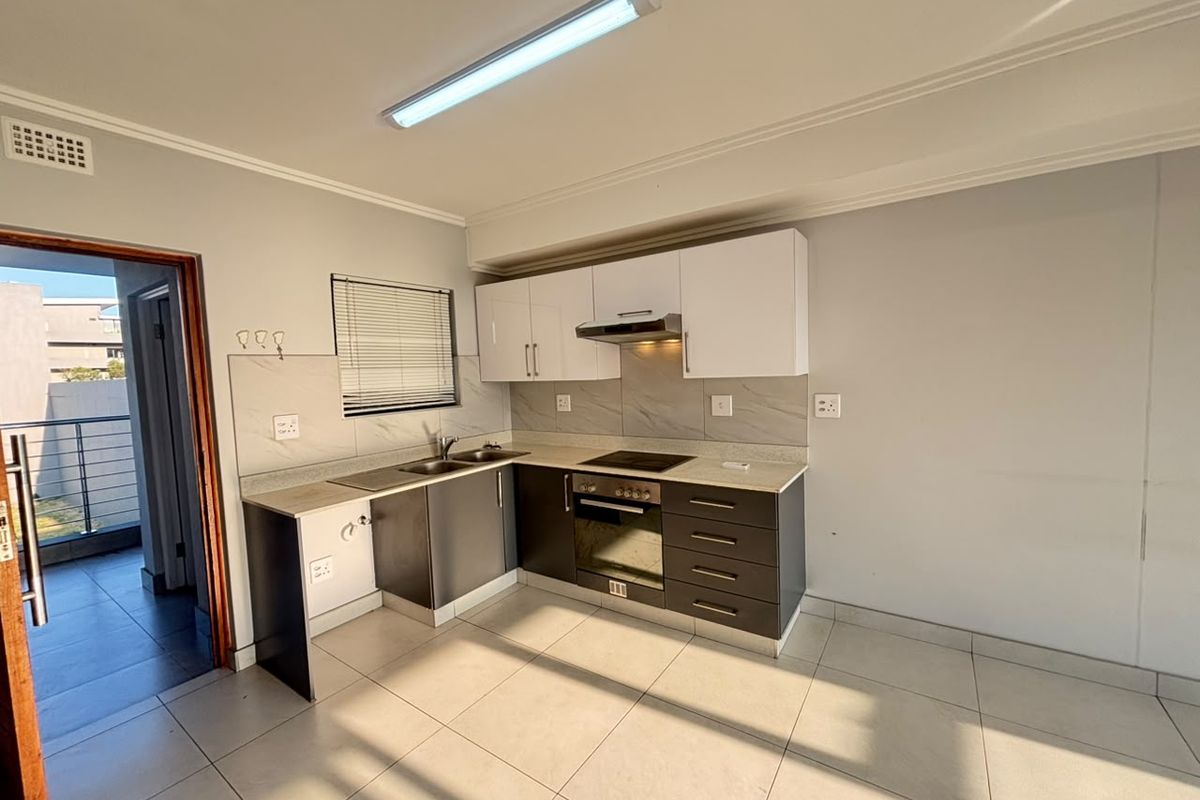 A clean, modern kitchen featuring two-tone cabinetry, stone countertops, integrated oven and hob, and tiled flooring, with direct access to an outdoor balcony area.