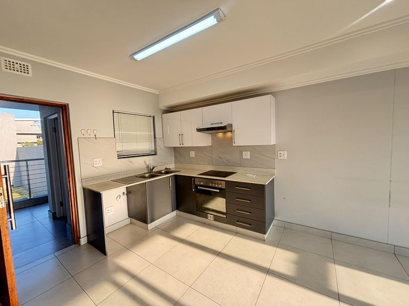 A clean, modern kitchen featuring two-tone cabinetry, stone countertops, integrated oven and hob, and tiled flooring, with direct access to an outdoor balcony area.
