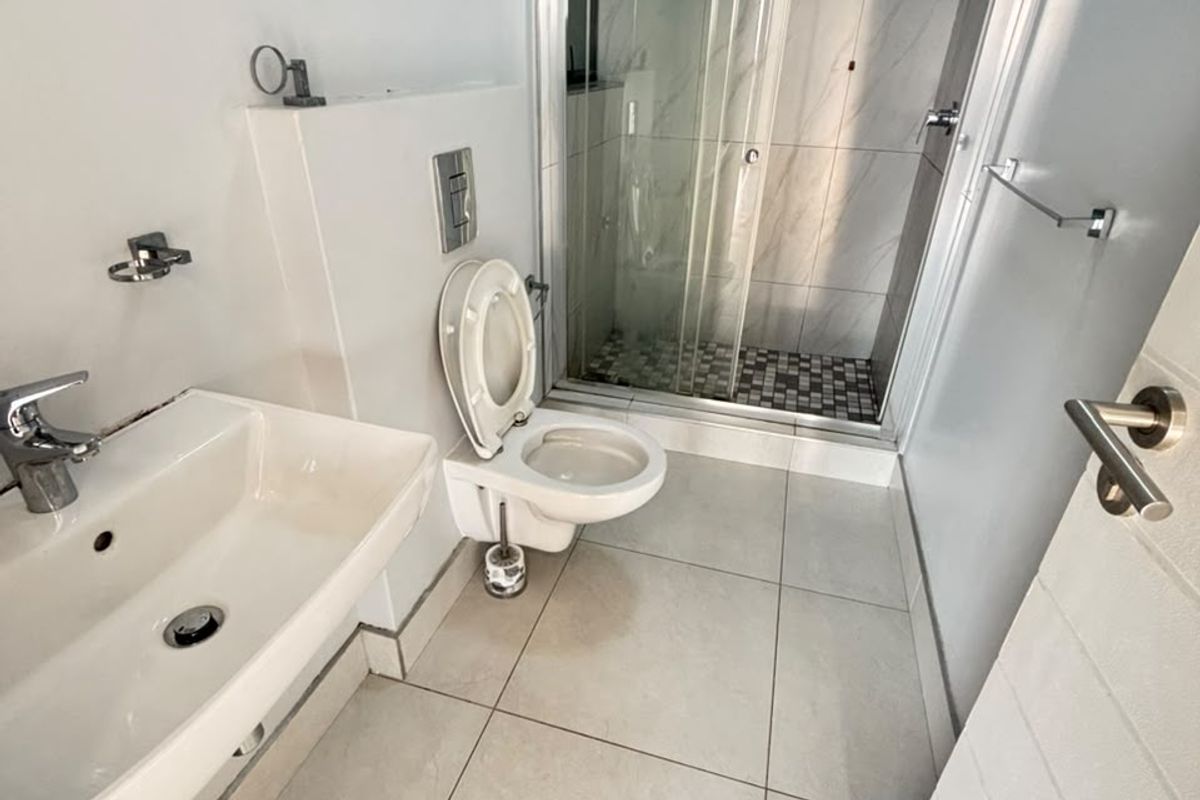 Modern bathroom featuring a wall-mounted toilet, glass shower enclosure, and wall-mounted basin with neutral tiled finishes throughout.
