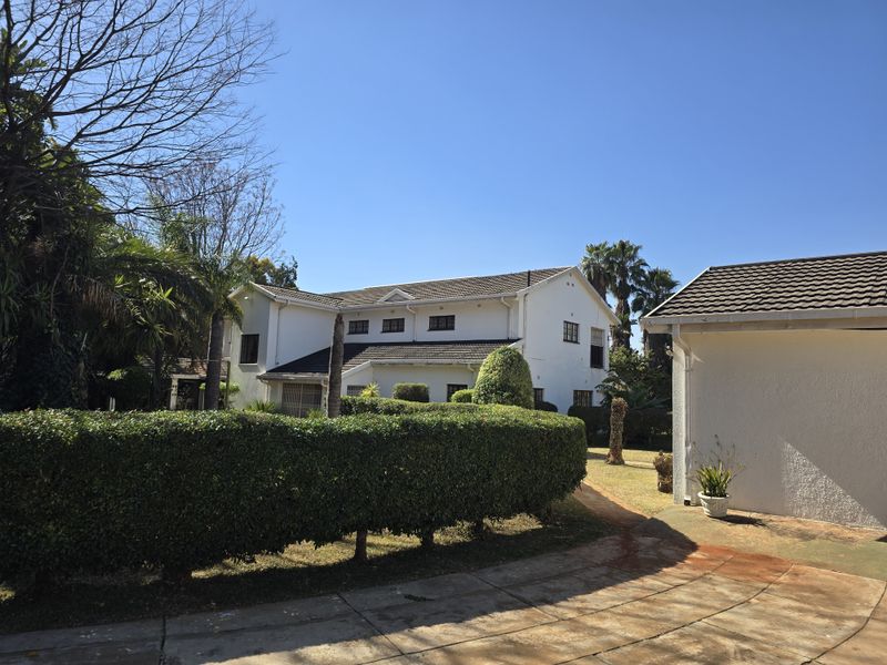 Rear view of a two-story residential property featuring a tiled roof, established garden with manicured hedges, and a detached garage.