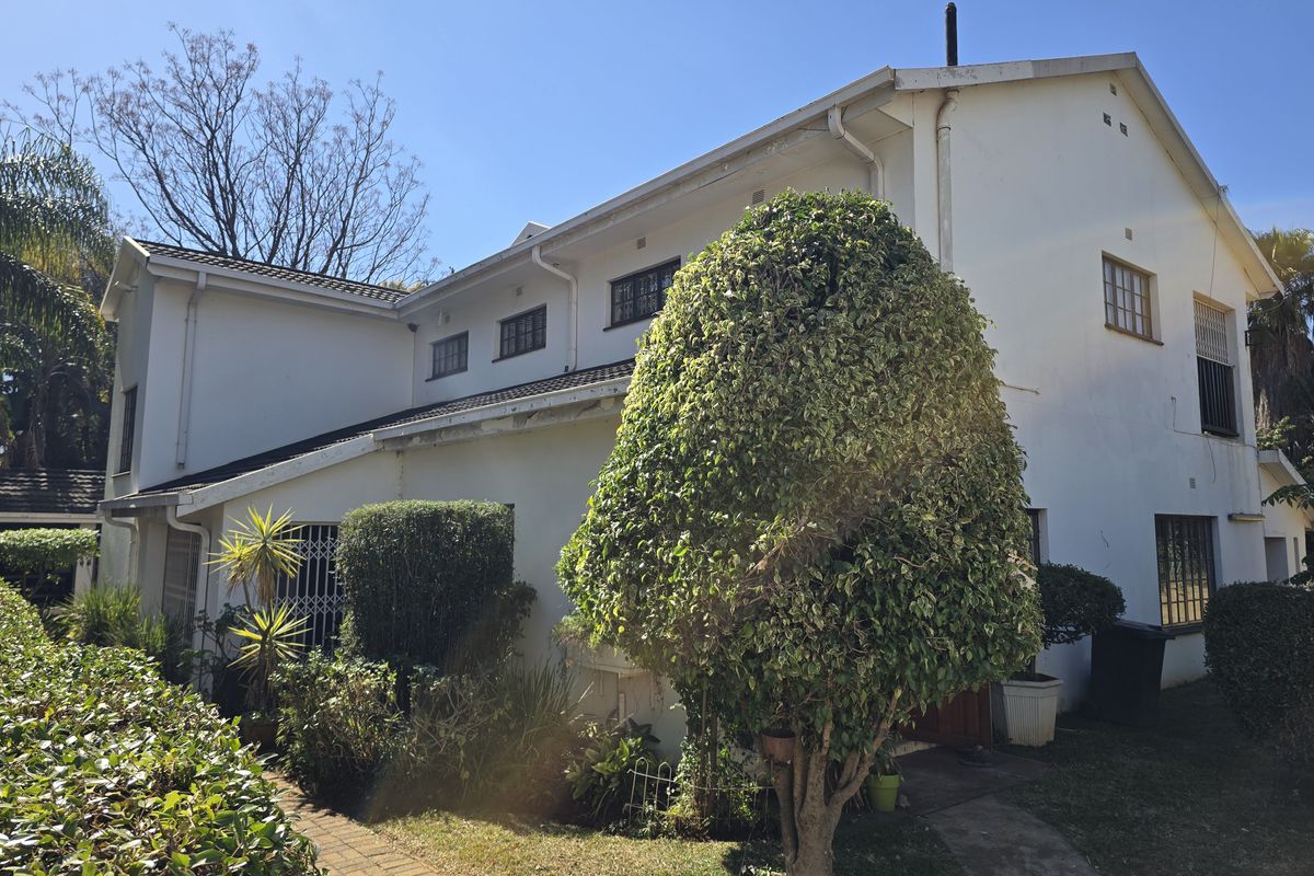Rear exterior view of a two-story house featuring white painted walls, security bars on windows, and a paved garden walkway.